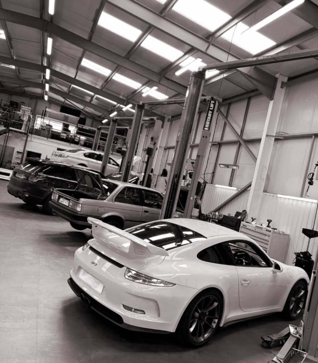 Four cars parked in garage workshop including a Porsche, BMW and Range Rover.